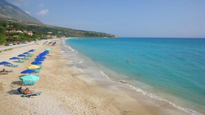 A beach with rows of blue and yellow umbrellas, a sandy shore, and a mountain in the background. - Panagis Villa - Three Bedroom Villa, Sleeps 6 (Karavados)