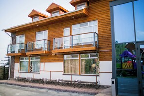 A two-story wooden building with balconies, large windows, and a paved entrance area. - Ethno Park Resort (Kok-Jar)