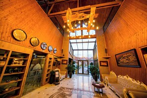 A lobby with wooden walls, a chandelier, clocks, a sofa, and a large window. - Ethno Park Resort (Kok-Jar)