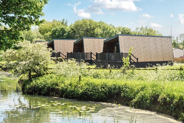 A row of wooden cabins with a deck and a view of a pond.