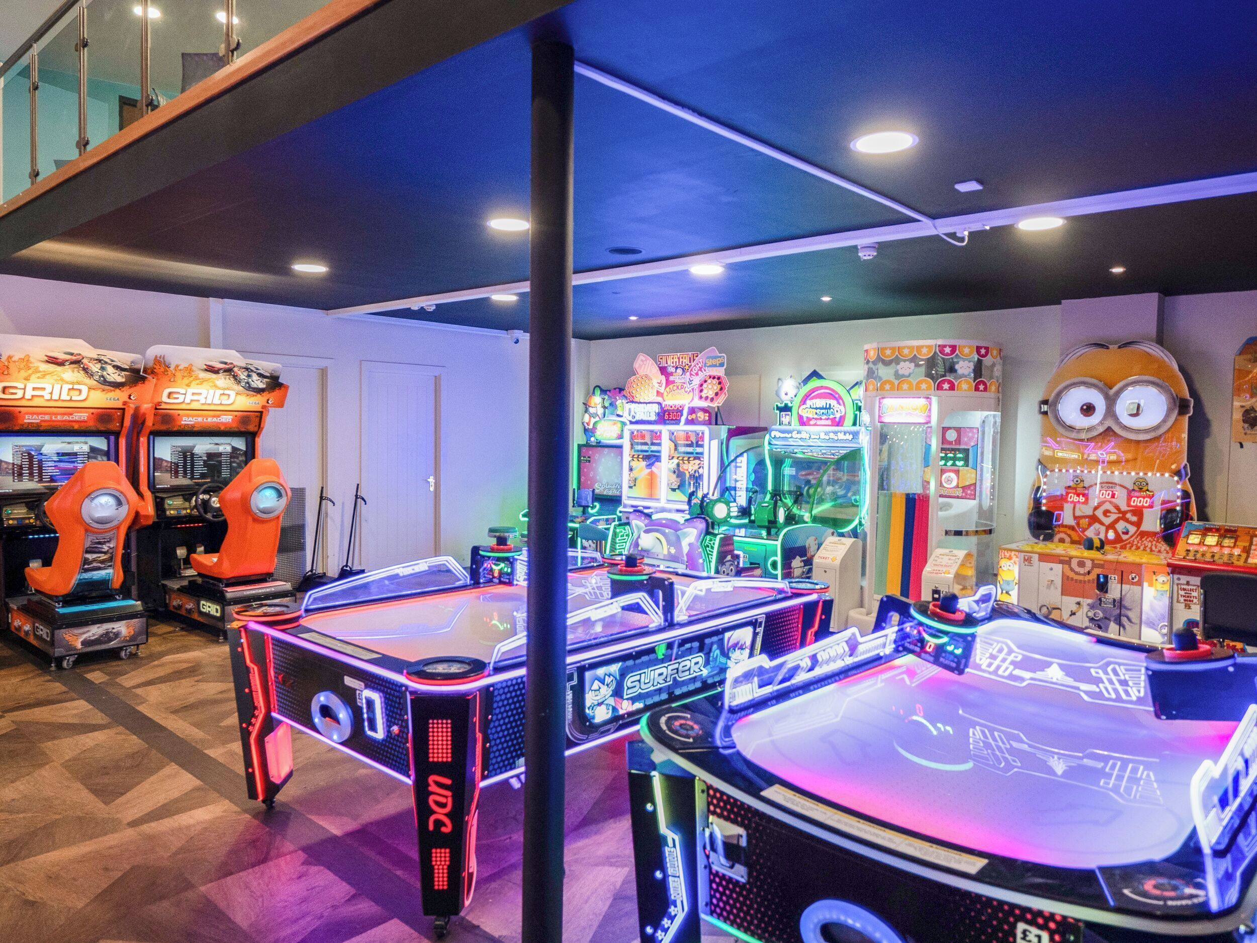 A gaming arcade with multiple arcade machines, including racing and fighting games, and a Minion-themed decoration.
