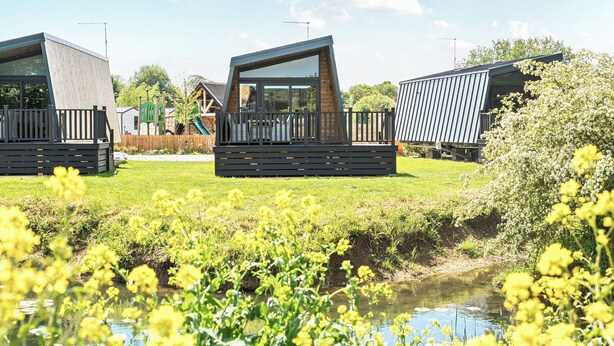 Een moderne camperpark met meerdere stacaravans, een klein waterpartij en een speeltuin op de achtergrond.