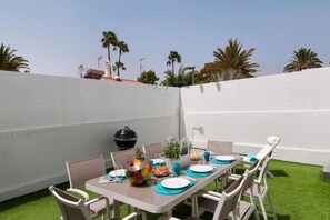 A patio with a table set for four, surrounded by chairs, a grill, and a small plant. - Bungalow JF/GI by VillaGranCanaria (Comarca Sur)