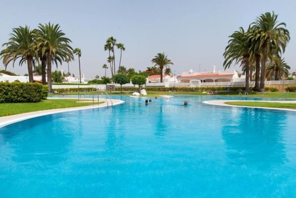 A large swimming pool with palm trees and a building in the background. - Bungalow JF/GI by VillaGranCanaria (Comarca Sur)