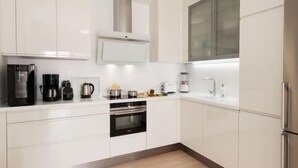 Μια σύγχρονη κουζίνα με λευκά ντουλάπια, εντοιχισμένο φούρνο, καφετιέρα και ένα  παράθυρο πάνω από τον νεροχύτη.