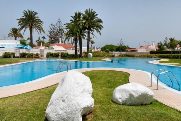 Ein Pool mit geschwungener Kante, umgeben von Rasen und Palmen.