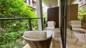 A balcony with wicker chairs and a glass table, overlooking a lush green area and adjacent buildings. - Ipana Siempre Playa Dowtown (Playa del Carmen)