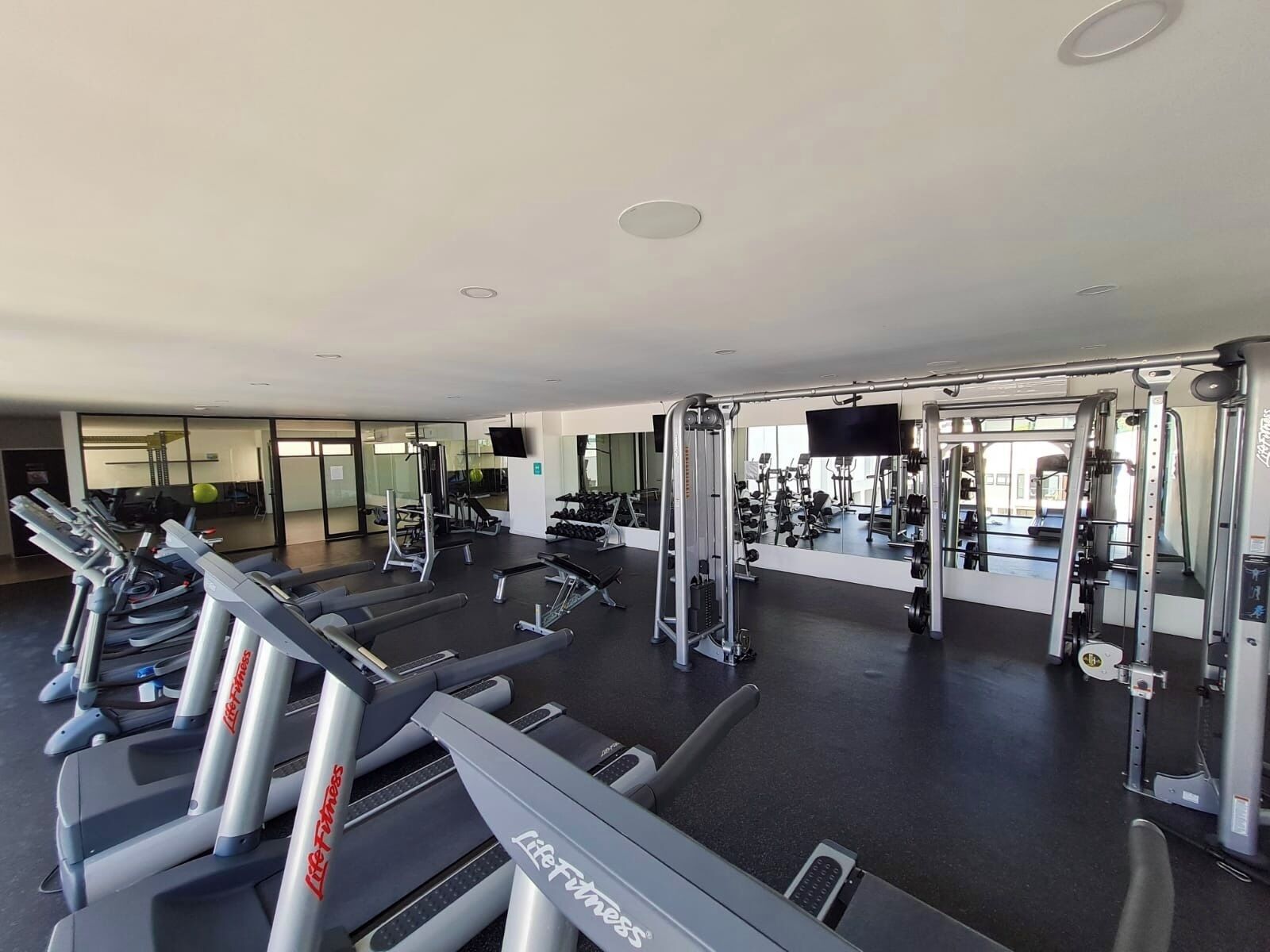 A gym with treadmills, weight machines, and a mirrored wall.