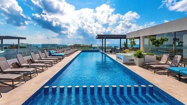 A rooftop infinity pool with lounge chairs, a glass balustrade, and a clear view of the city skyline. - Ipana Siempre Playa Dowtown (Playa del Carmen)