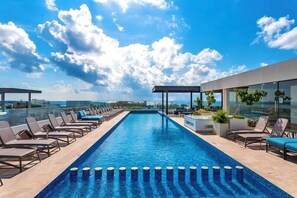 Ein Dachpool mit unendlicher Optik, Liegestühlen, einer Glasbrüstung und freiem Blick auf die Stadtlandschaft.