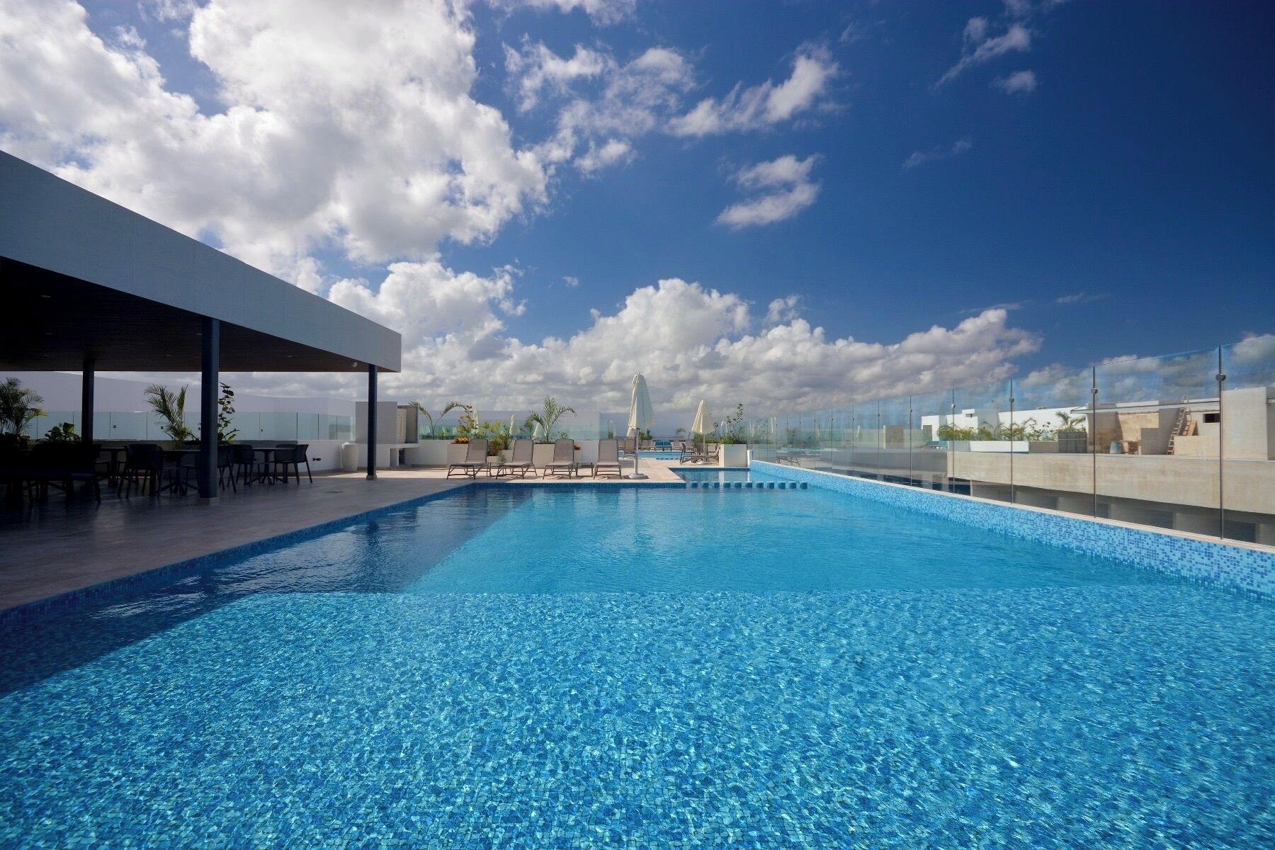 A rooftop swimming pool with clear blue water, lounge chairs, and umbrellas.