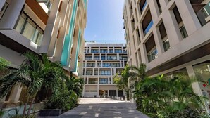 A modern building with multiple floors, large windows, and a central courtyard with palm trees. - Ipana Siempre Playa Dowtown (Playa del Carmen)
