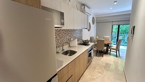 A modern kitchen with a built-in refrigerator, a microwave, and a stove. There is a dining area with a table and chairs, and a large window providing a view of greenery outside. - Ipana Siempre Playa Dowtown (Playa del Carmen)