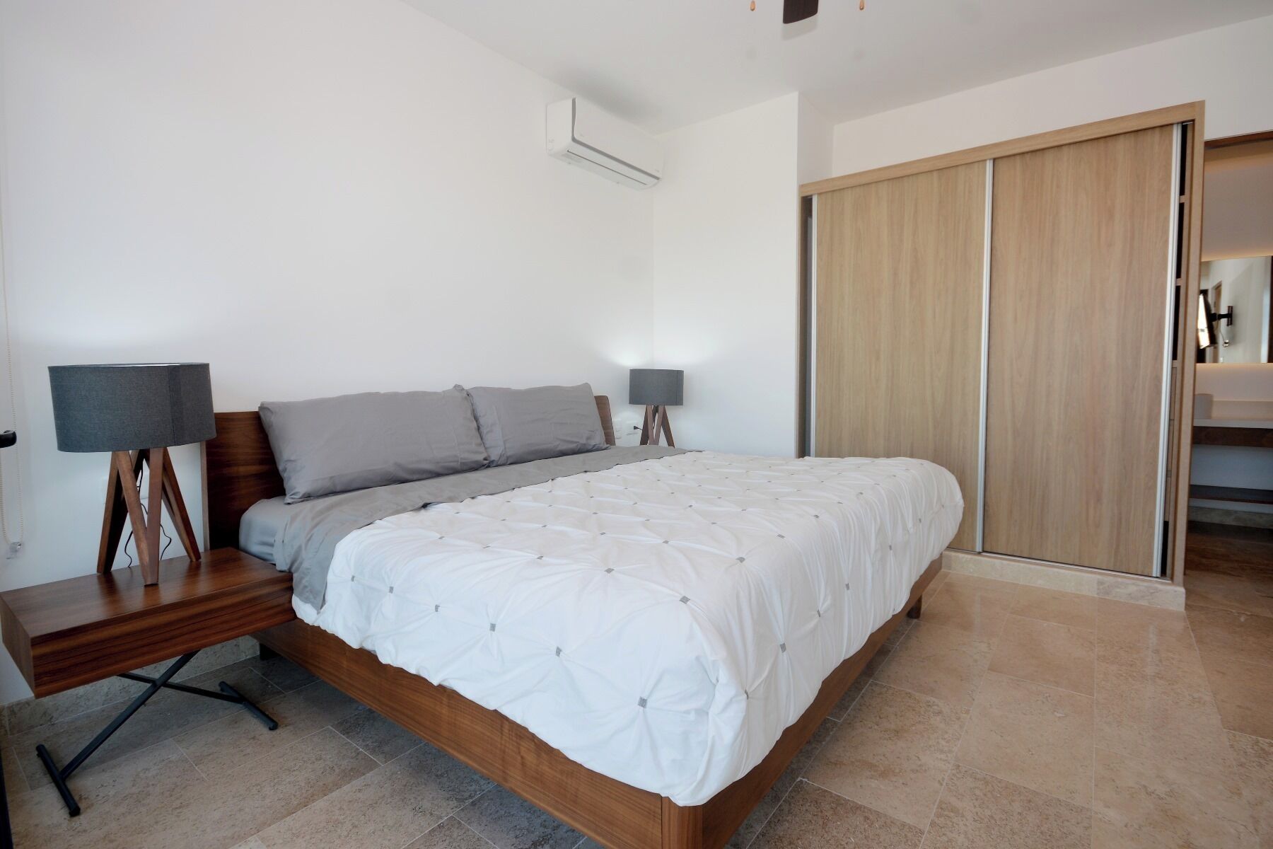 A bedroom with a wooden bed, two bedside tables with lamps, a wardrobe, and a bathroom visible through an open door.