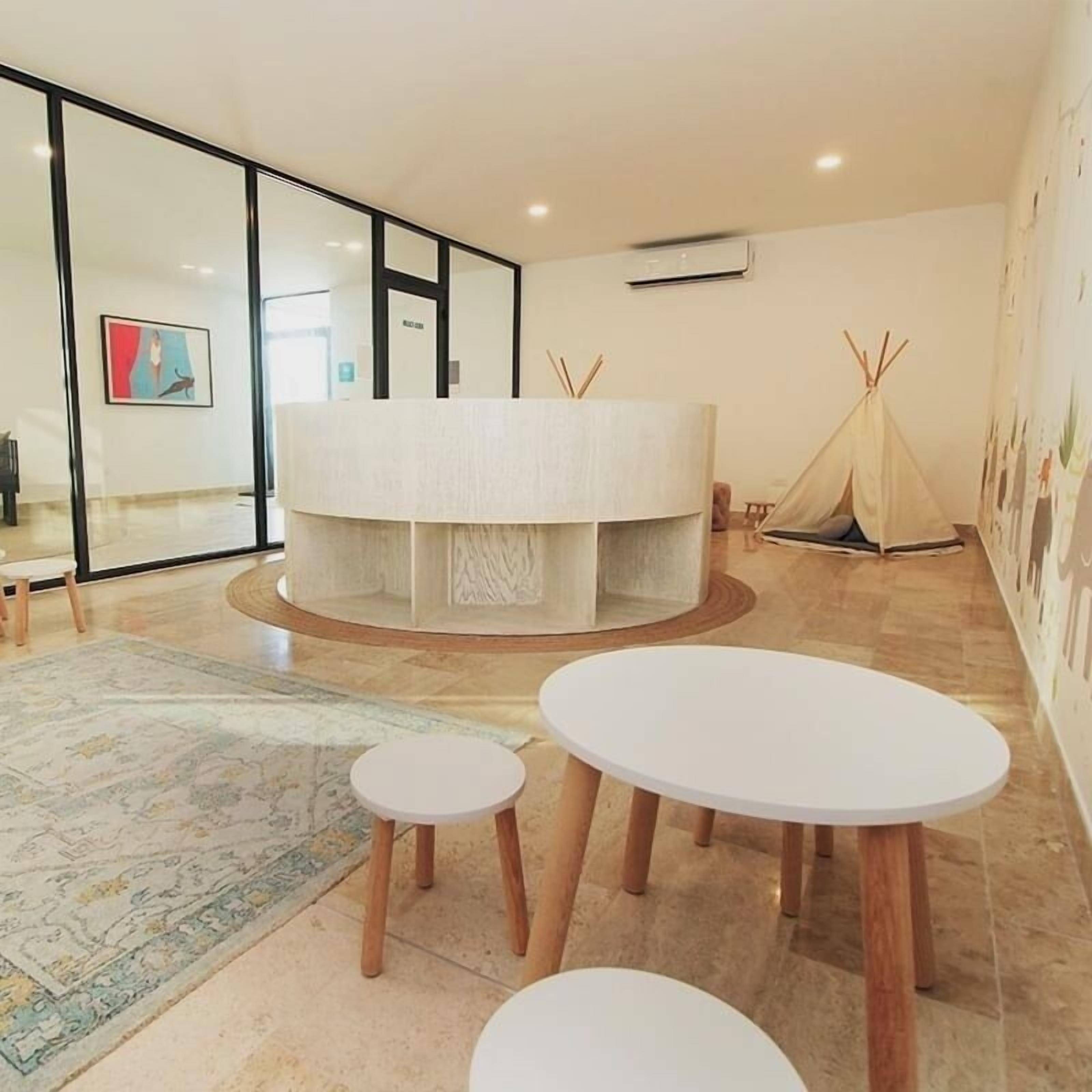 A modern, minimalist room with a central round table, two smaller round tables, a patterned rug, and a tent-like structure against the wall.