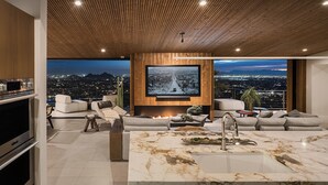 Una sala de estar moderna con un televisor grande, asientos cómodos, una zona de cocina y vistas a la ciudad.