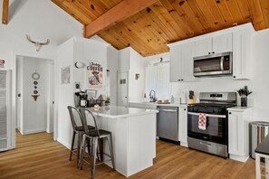 Een moderne keuken met witte kasten, een centraal eiland, een magnetron, een fornuis en een koffiehoek.