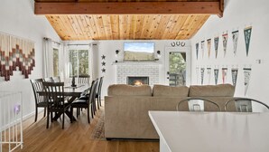 Een moderne woonkamer met een open haard, houten plafond, een eethoek en uitzicht op de omgeving.
