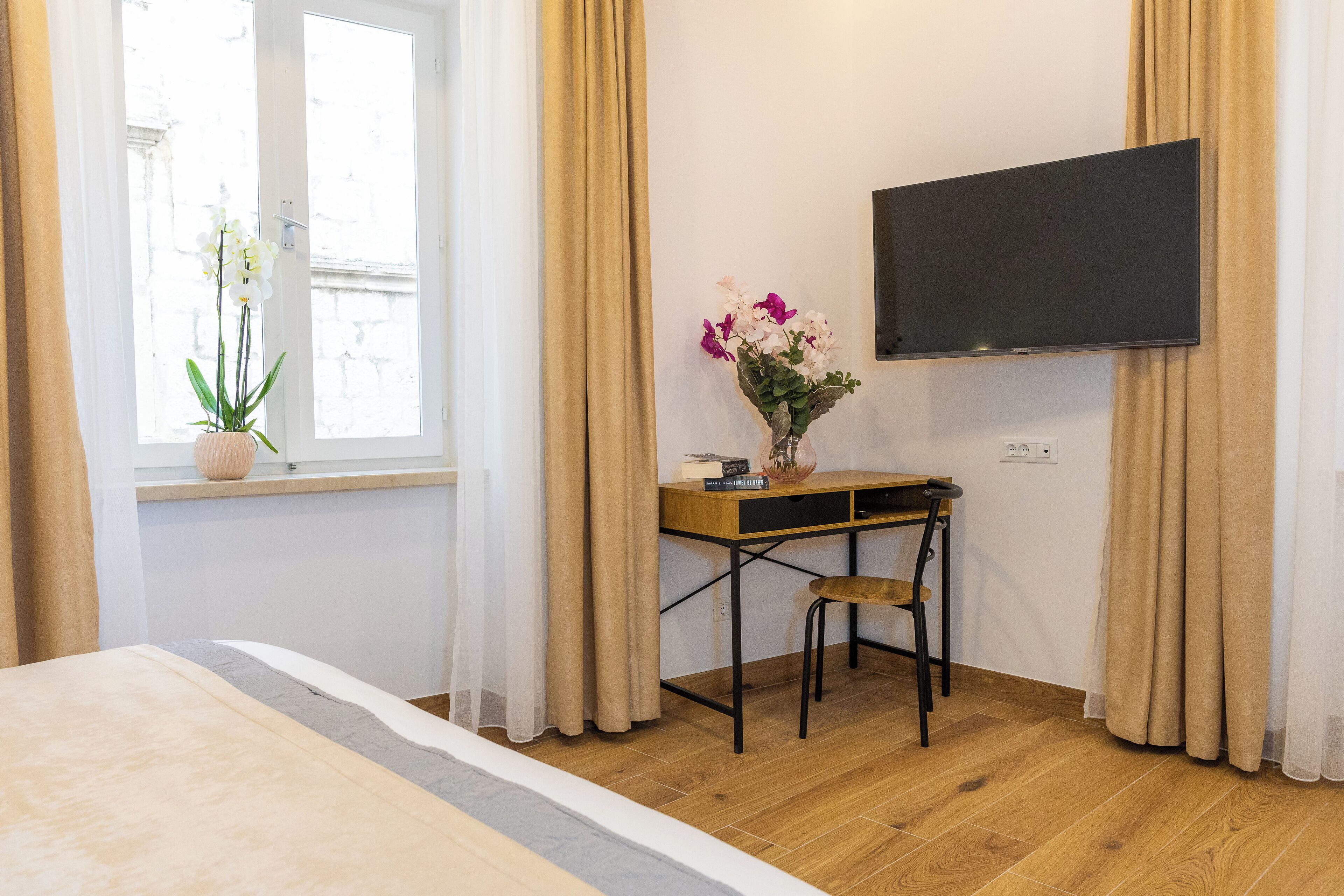 A hotel room with a bed, a desk with a chair, a TV, and a window with curtains.