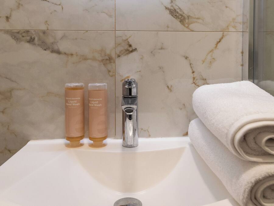 A bathroom with a marble sink, two bottles of liquid hand wash, a faucet, and a rolled towel.