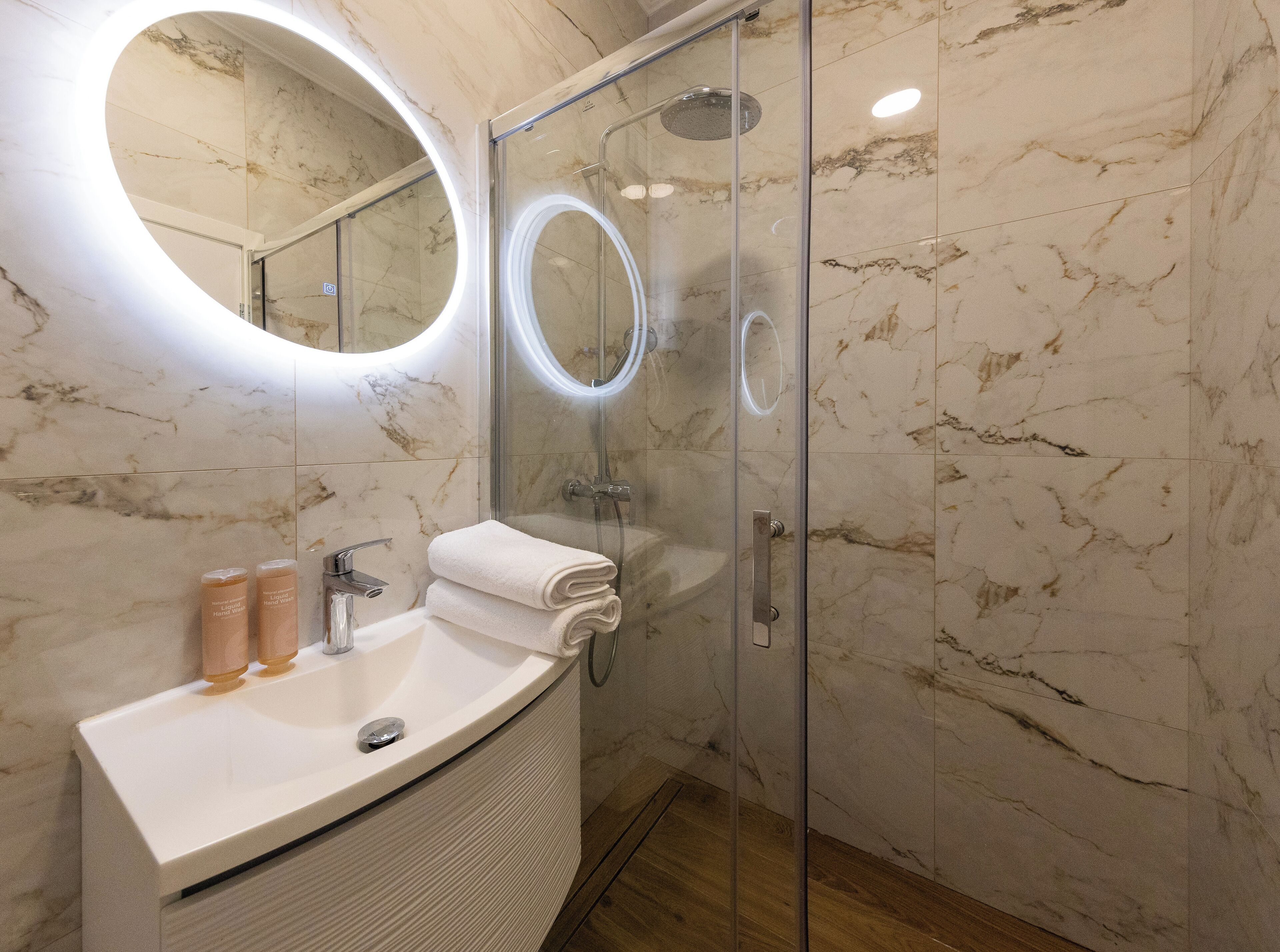 A modern bathroom with a marble vanity, a glass-enclosed shower, and a round mirror.