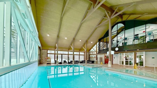 An indoor swimming pool with clear water, surrounded by a high ceiling and large windows.