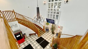 A spacious interior with a wooden staircase, a chandelier, a checkered floor, and a large window.