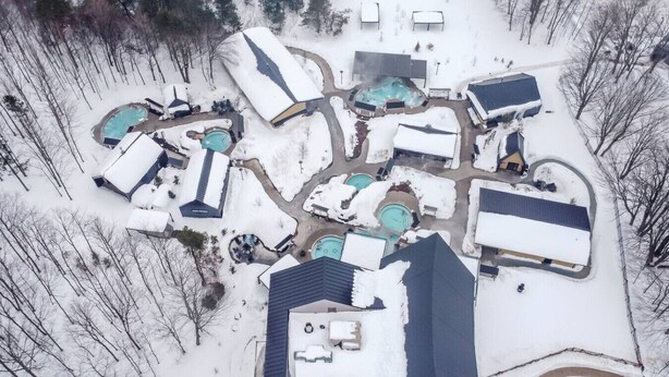 Vista aérea de un complejo turístico con múltiples piscinas, pasillos cubiertos y edificios rodeados de nieve.