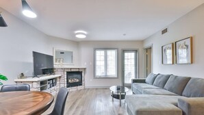 A modern living room with a fireplace, a dining area, and a sofa. - Hideaway 2BR Condo Pool & Heated Pool (Shanty Bay)