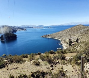A coastal landscape with a large body of water, a small island, and a hilly terrain. - Kalluchi Ecolodge SunIsland TiticacaLake (Isla del Sol)