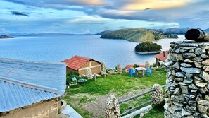 A lakeside property with a stone wall, a small building with a red roof, and a grassy area with blue chairs. - Kalluchi Ecolodge SunIsland TiticacaLake (Isla del Sol)