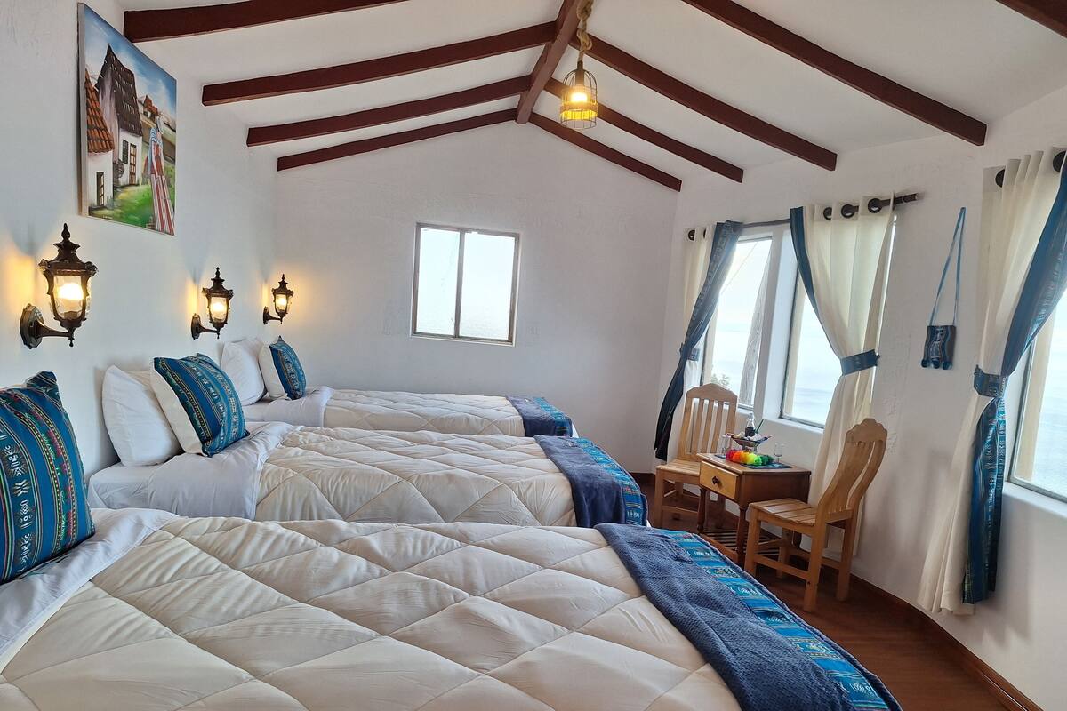 A bedroom with two beds, wooden beams, a window, and a small table with a chair.