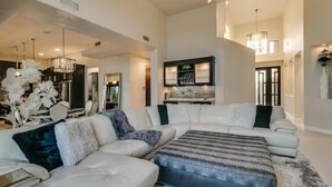 A spacious living room with a large sectional sofa, a chandelier, and a modern kitchen in the background. - Luxury Contemporary Sanctuary w/  Pool and Views! (Fountain Hills)