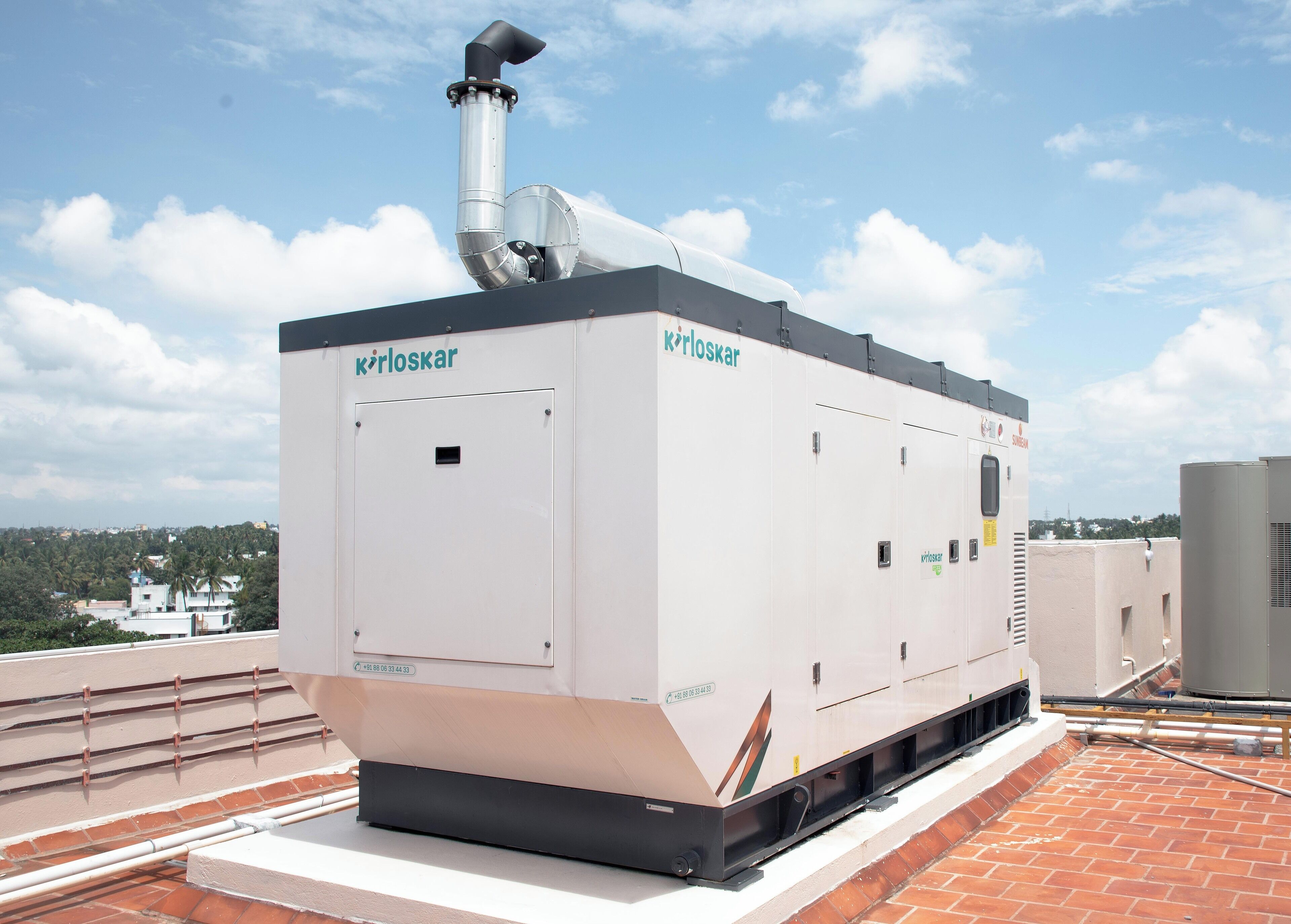 A rooftop air conditioning unit with the brand 'körloskar' on a building with a clear sky and distant trees.