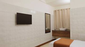 Une salle de bain d’hôtel avec un grand miroir, un lavabo, des toilettes et un lit recouvert d’une couverture orange.