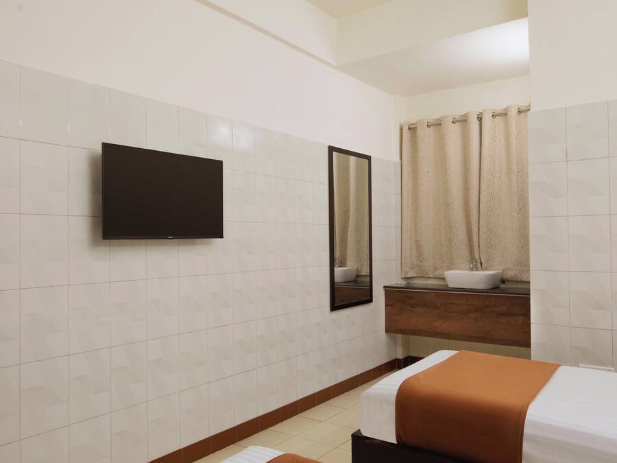 Une salle de bain d’hôtel avec un grand miroir, un lavabo, des toilettes et un lit recouvert d’une couverture orange.