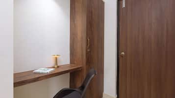 Quarto com guarda-roupa de madeira, uma pequena prateleira com um livro e uma lâmpada, e uma cadeira preta.