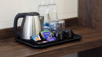 A tray with a kettle, bottled water, coffee cups, and tea packets on a wooden counter.