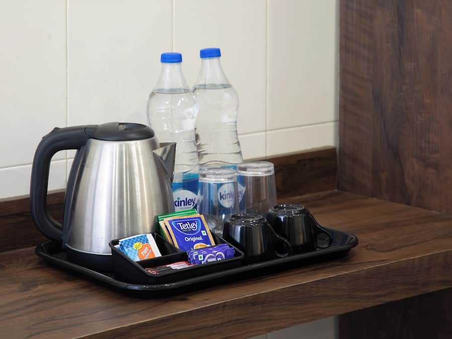 A tray with a kettle, bottled water, coffee cups, and tea packets on a wooden counter.