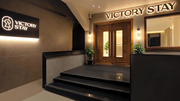 Een hotelingang met een bord waarop 'VICTORY STAY' staat, en een modern ontwerp met een trap naar de deuren.