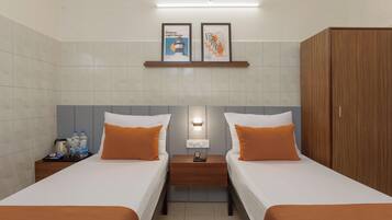 A hotel room with two beds, a wooden wardrobe, a nightstand with a phone, and a shelf with framed artwork.