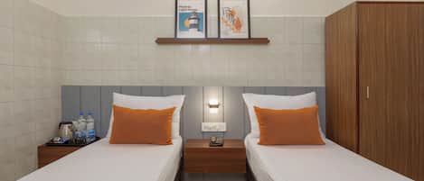Habitación de hotel con dos camas, un armario de madera, una mesita de noche con un teléfono y una estantería con obras de arte enmarcadas.