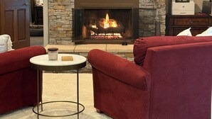 Ein Wohnzimmer mit Kamin aus Stein, roten Sofas, einem kleinen runden Tisch und Holzboden.