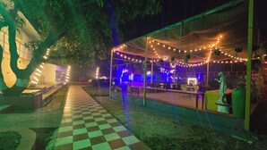 An outdoor area with a checkered pathway leading to a covered seating area with string lights and a statue. - SAAZ RESORT AND LAWN (Khalapur)