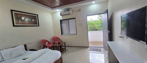A bedroom with a bed, a ceiling fan, a TV, and a window with a view of greenery.