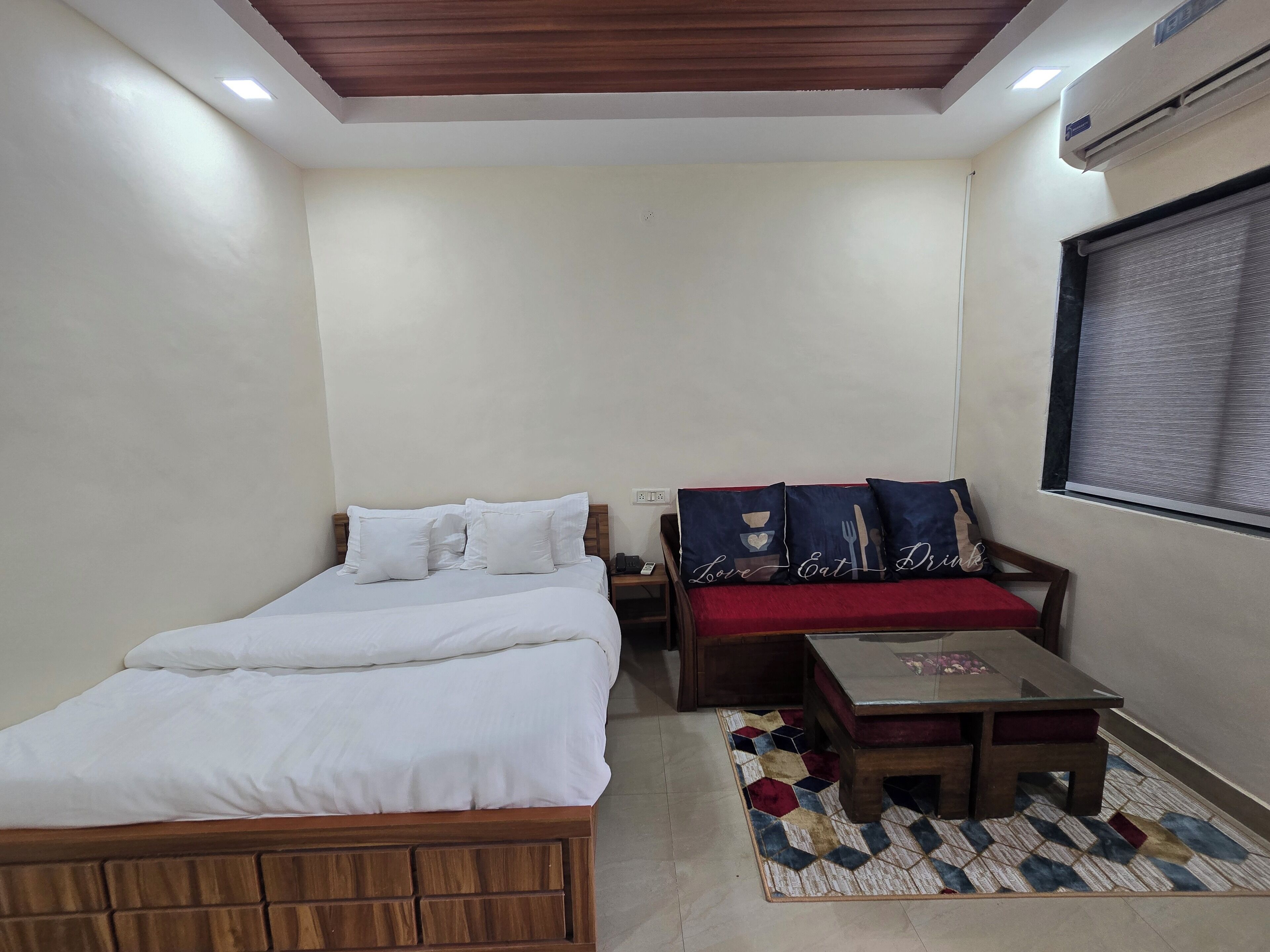 A bedroom with a bed, a sofa, a small table, and a window with blinds.