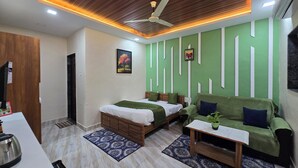 A modern hotel room with a wooden ceiling, a bed with green bedding, a green sofa, a small table, and a ceiling fan. - SAAZ RESORT AND LAWN (Khalapur)