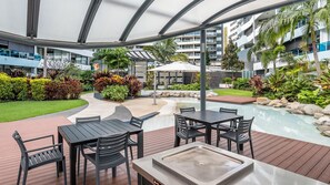 An outdoor patio area with a pool, surrounded by lush greenery and modern buildings in the background. - Riverside at WaterEdge West End (West End)