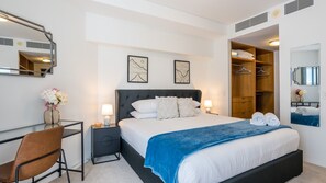 A modern hotel room with a large bed, a desk, a chair, and a wardrobe. - Riverside at WaterEdge West End (West End)