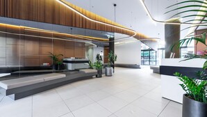 A modern reception area with a curved wooden panel design, a reception desk, and potted plants. - Wellness and Style - 2BR Apartment with Pool, Hot Tub and Gym (Moonee Ponds)
